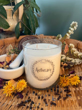 Load image into Gallery viewer, Candle labeled 'Apothecary' on a woven mat with flowers and herbs