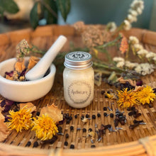 Load image into Gallery viewer, Mason jar candle labeled 'Apothecary' on a woven mat with dried flowers and herbs