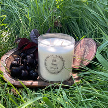 Load image into Gallery viewer, Candle labeled &#39;Dark Cherry Orchard&#39; on a wooden coaster with cherries and leaves in grass