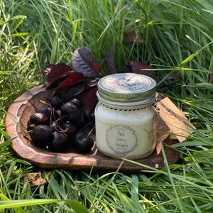 "Dark Cherry Orchard" candle on a wooden plate with cherries in grass
