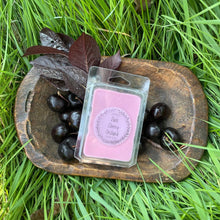 Load image into Gallery viewer, Pink &quot;Dark Cherry Orchard&quot; wax melt in a clear container on a wooden tray with cherries and leaves, placed on grass.